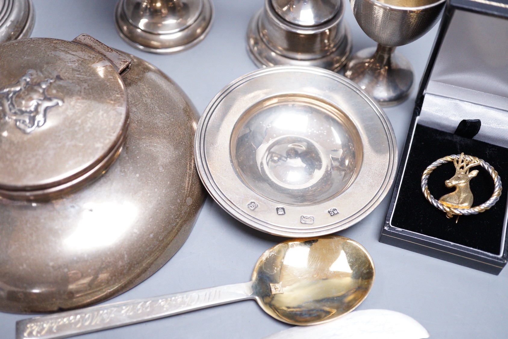 A small collection of assorted small silver, including a capstan inkwell, pair of dwarf candlesticks, two small trophy cups, egg cup, flatware, napkin ring, glass caster, a modern parcel gilt silver stag brooch and three